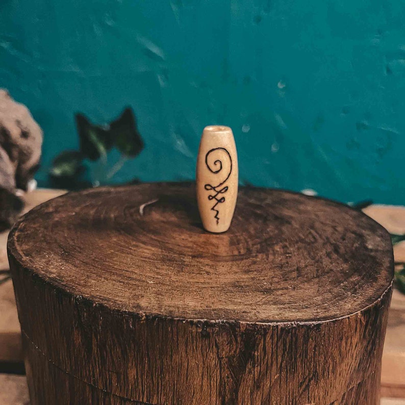 May include: A wooden bead with a black and white symbol carved into it. The bead is sitting on a wooden surface.