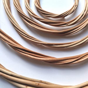 May include: A set of three concentric circular wreaths crafted from natural light brown willow branches. The wreaths are arranged in a nested pattern, showcasing the smooth, woody texture and flexible, intertwined structure of the organic material.