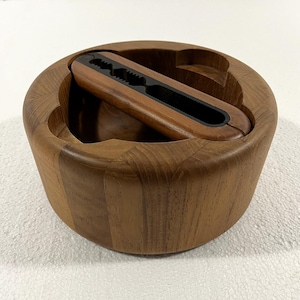 May include: A wooden nutcracker set. The set includes a round bowl with three curved cutouts and a matching nutcracker. The nutcracker is brown with a black interior. The bowl and nutcracker are made of wood.