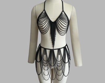 Puede incluir: Un arnés de cuerpo de malla de cadena negra con un top halter y una falda. La malla de cadena está hecha de pequeños anillos de metal unidos.