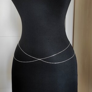 May include: A silver body chain with two strands that cross in the front. The chain is worn on a black mannequin.