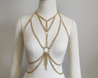 May include: Gold chain body jewelry with multiple layers and a circular pendant. The chain is made of a delicate, linked design.