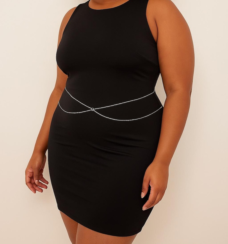 May include: A black sleeveless dress with a silver chain body jewellery piece. The chain is double layered and has a circular design in the centre.