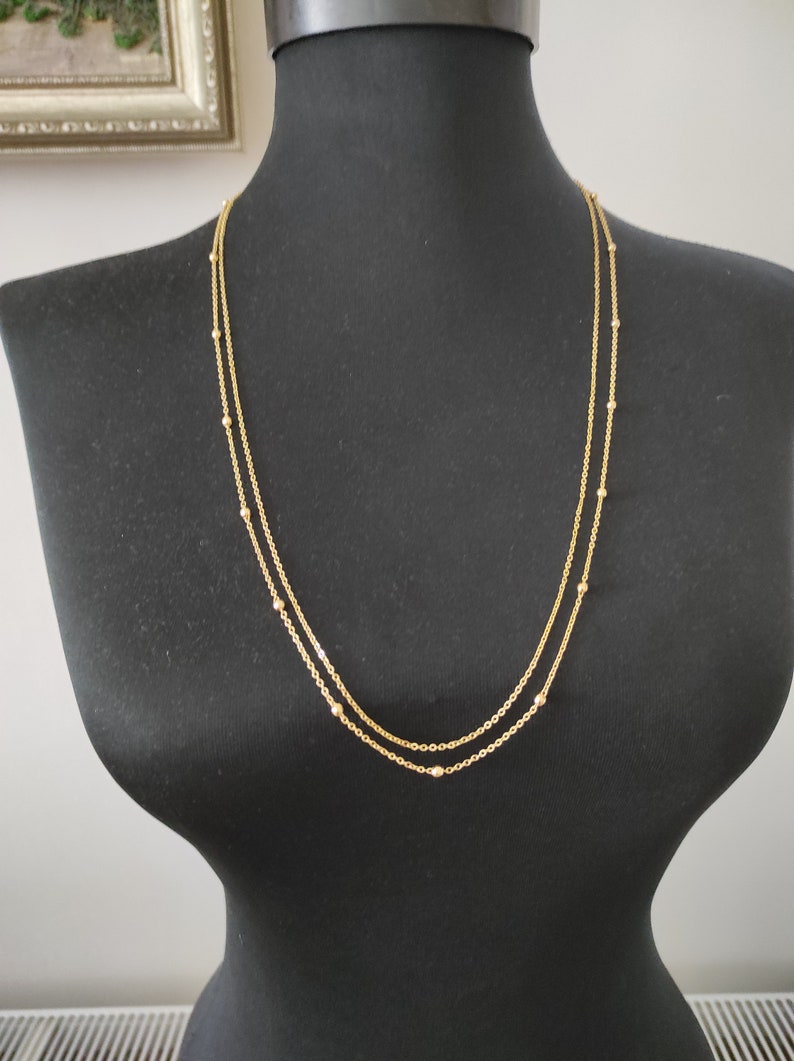 May include: A gold chain necklace with small beads. The necklace is layered, with one chain slightly longer than the other.