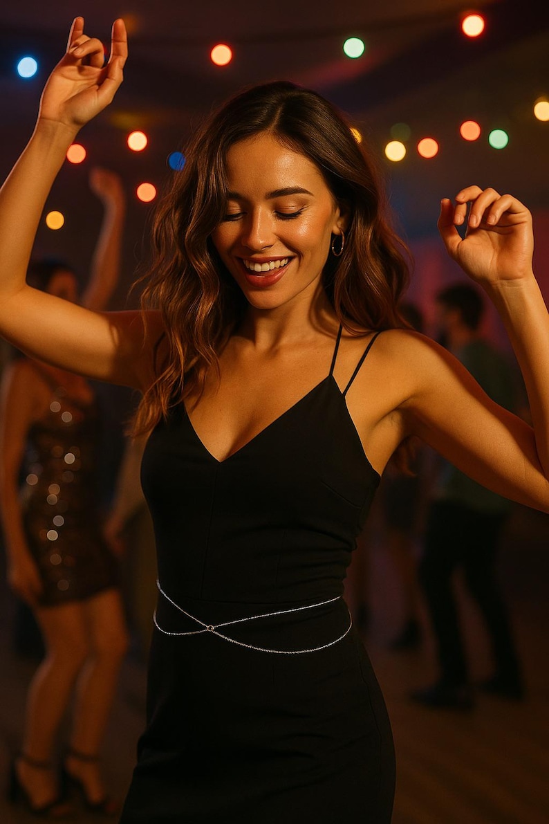 May include: A woman in a black dress with a silver chain belt dances at a party with string lights in the background.