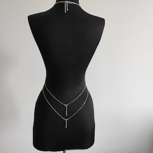 Op de afbeelding: Een zilveren body chain met twee strengen en een hangende hanger. De ketting wordt getoond op een zwart mannequins.