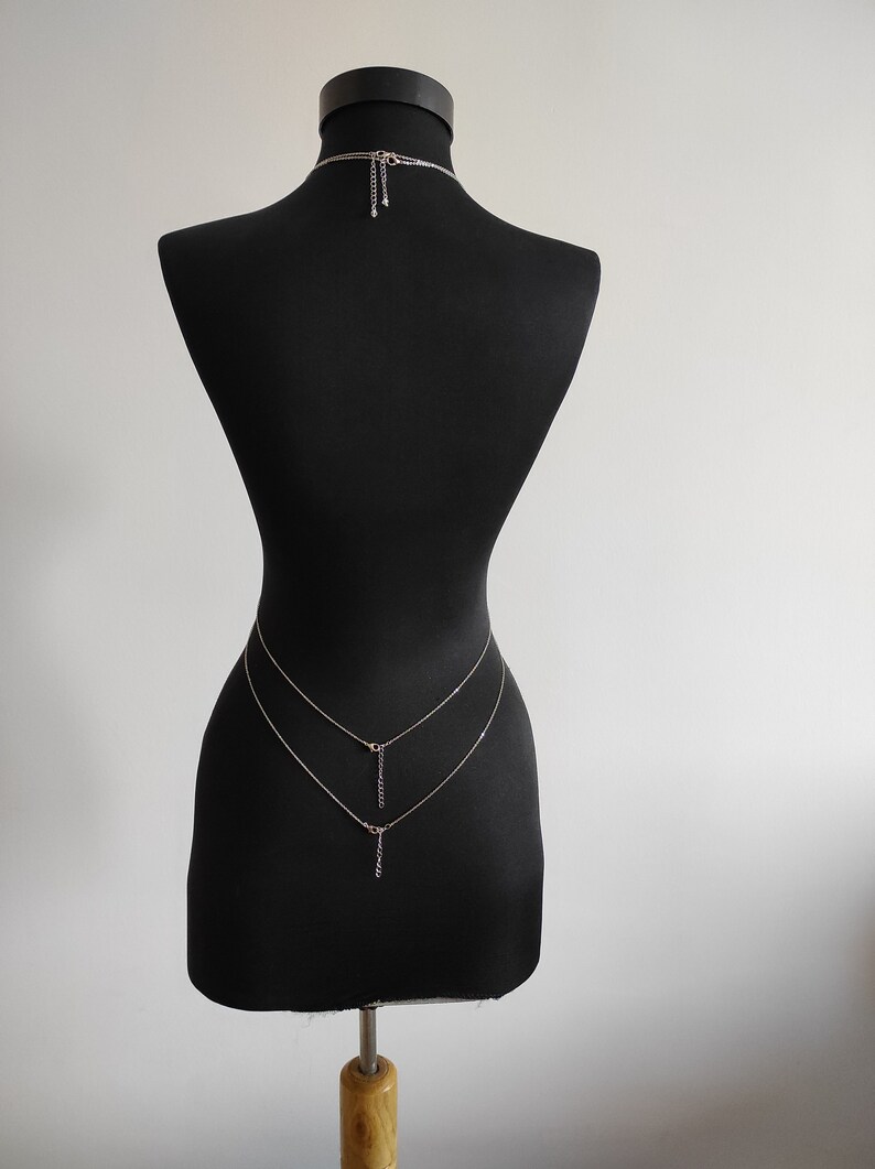 Op de afbeelding: Een zilveren body chain met twee strengen en een hangende hanger. De ketting wordt getoond op een zwart mannequins.