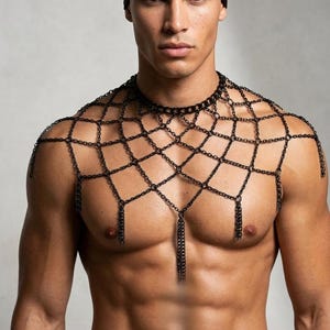 Op de afbeelding: Een zwart maliënkolderlichaamsharnas met een geometrisch ontwerp. Het harnas heeft een choker-stijl halslijn en kettingkwasten. Het model draagt een zwarte hoofdbekleding.