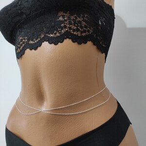 May include: A silver body chain with two strands, worn on a mannequin with a black lace top and black bottoms.