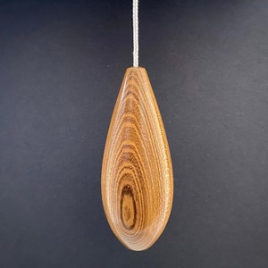 May include: A wooden light pull with a teardrop shape and a natural wood grain finish.