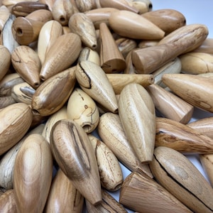 Op de afbeelding: Een verzameling gedraaide houten knoppen in verschillende bruin- en beigetinten. De knoppen hebben een gladde, gepolijste afwerking en verschillende vormen, waaronder druppel- en cilindervormen. De houtnerf is zichtbaar.