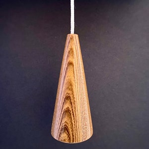 May include: A wooden light pull with a cone shape and a natural wood grain finish.