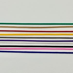 May include: A collection of colorful cords in various shades, including green, tan, red, yellow, gray, purple, white, black, pink, and blue. These cords are arranged horizontally against a white background, showcasing their diverse hues.