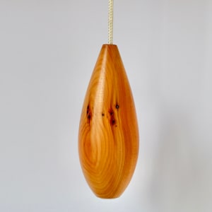 Puede incluir: Un tirador de luz de madera con forma de lágrima. El tirador está hecho de madera marrón claro con un patrón de veta natural.