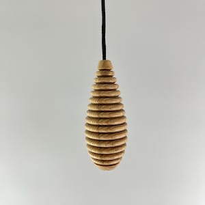 Puede incluir: Un tirador de luz de madera con un diseño en espiral. El tirador es de color marrón claro y tiene un cordón negro.