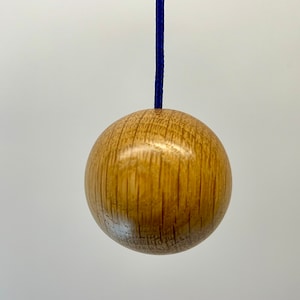 Könnte beinhalten: Ein Holz-Lichtschalter mit einer runden, hellbraunen Kugel und einem dunkelblauen Kabel.
