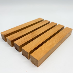 May include: Five rectangular wooden blocks, light brown in colour with visible wood grain, are arranged on a white surface. The blocks are evenly spaced, showcasing their natural texture and shape. The wood appears freshly cut.