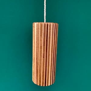 May include: A wooden light pull with a striped pattern in shades of brown and beige. The pull is hanging from a white cord against a teal green background.