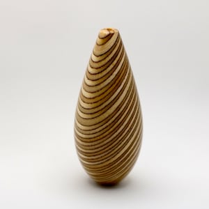 May include: A teardrop-shaped wooden vase with a swirling, striped pattern in shades of brown and beige.