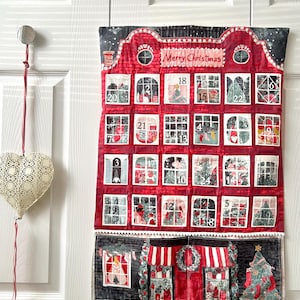 May include: A red and black Christmas advent calendar with the words "Merry Christmas" across the top. The calendar has 24 numbered windows with festive images. It is hanging on a white door.