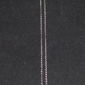 May include: Silver-toned necklace with a round pendant. The pendant features a detailed design with a mix of silver, gold, and red accents. The chain is a delicate, linked style.