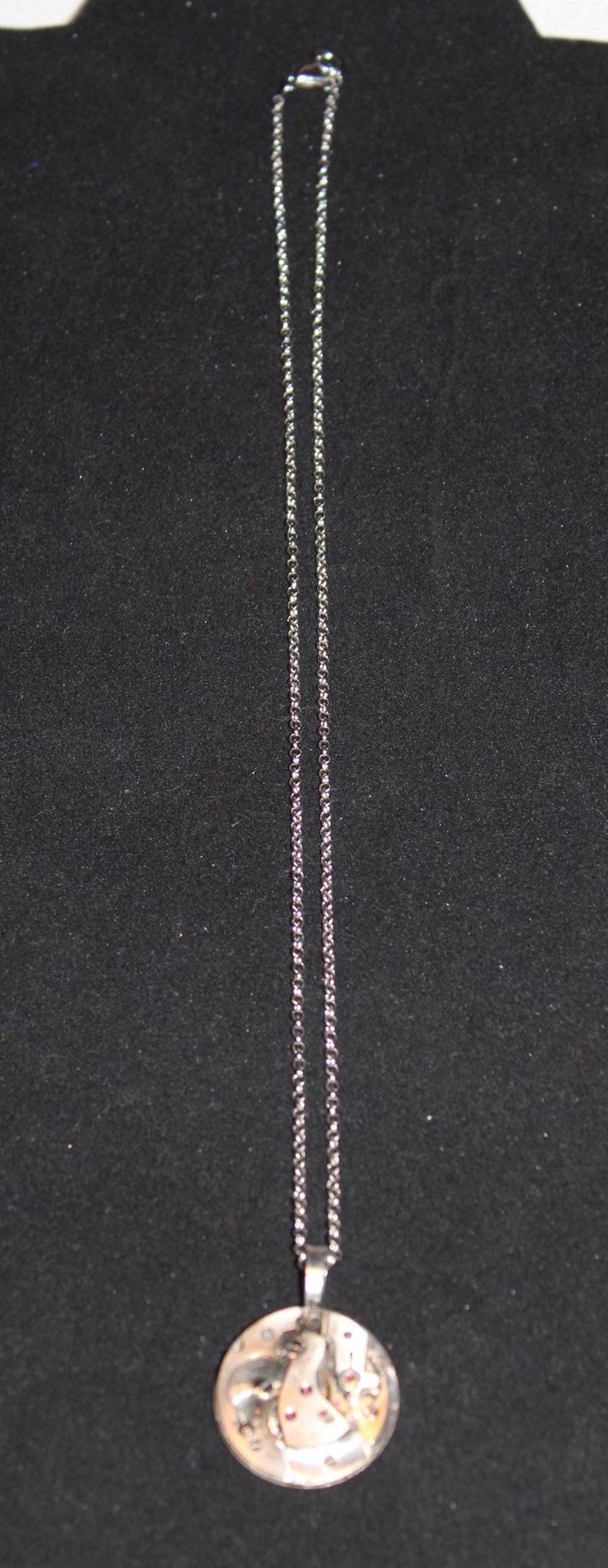 May include: Silver-toned necklace with a round pendant. The pendant features a detailed design with a mix of silver, gold, and red accents. The chain is a delicate, linked style.