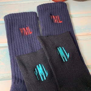 May include: Two pairs of socks, one navy blue and one black, with embroidered initials. The navy socks have red "YML" initials, while the black socks feature teal initials. The socks are folded, showing the embroidered initials.