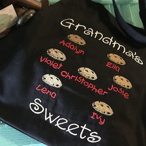 May include: Black tote bag with the text "Grandma's Sweets" embroidered in white. The bag features a cookie tree with the names of family members, including Adalyn, Violet, Christopher, Lena, Ella, Josie, and Ivy, embroidered in red.