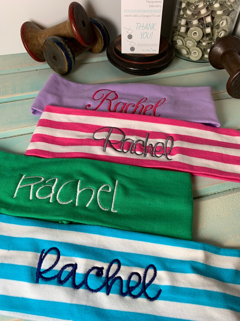 Pu&ograve; includere: Quattro fasce per capelli con il nome "Rachel" ricamato su di esse in diversi colori e font. Le fasce sono impilate l'una sull'altra. La fascia superiore &egrave; viola, la seconda &egrave; a righe rosa e bianche, la terza &egrave; verde e l'ultima &egrave; a righe blu e bianche.