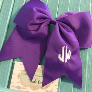 May include: Purple cheer bow with a white embroidered monogram "JW".