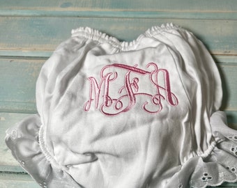 以下が含まれることがあります： ピンクの刺繍モノグラムが入った白いベビーブルマ。 ブルマは、フリル付きのウエストと脚の周りにアイレットレースのトリムが付いています。 生地は柔らかく、軽量で、赤ちゃんに適しているようです。