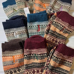 May include: A collection of colorful, patterned socks with embroidered letters. The socks feature a variety of colors, including teal, navy, burgundy, and orange, with geometric and tribal-inspired designs. Each sock has a different letter embroidered on it.