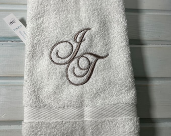 May include: White hand towel with a brown embroidered monogram of the letter "J".