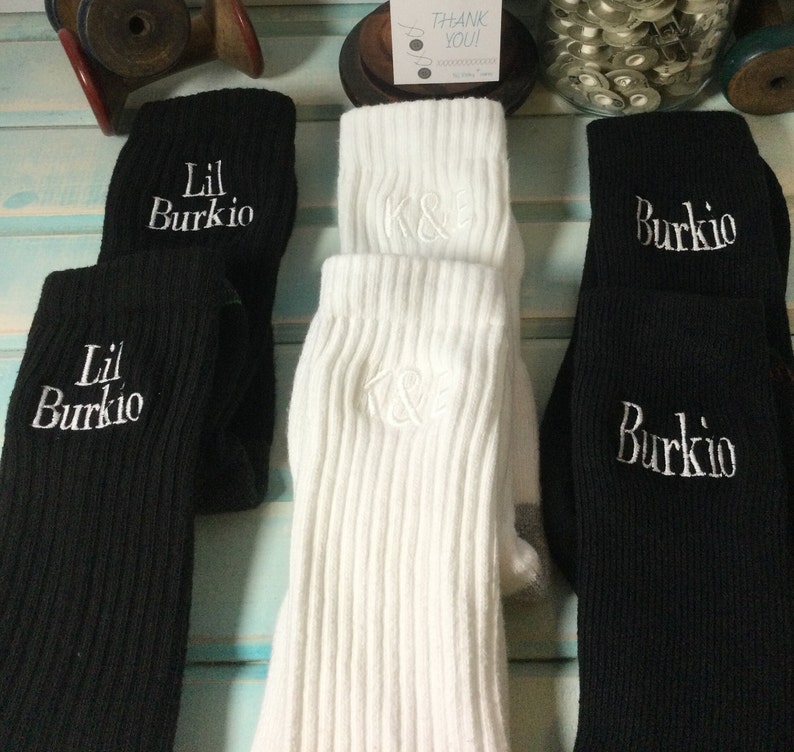 May include: A collection of ribbed knit socks in black and white. The black socks are embroidered with "Lil Burki0" and "Burkio" in white. The white socks are embroidered with "K&E" in white. The socks are folded over.