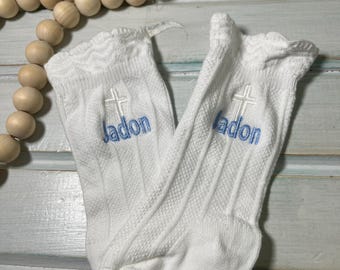 May include: A pair of white knee-high socks with a blue cross and the name "Jadon" embroidered on each sock.