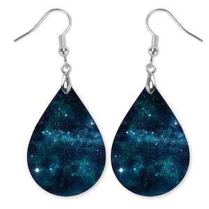 May include: A pair of teardrop-shaped earrings with a galaxy print. The earrings are silver and have a dark blue background with white stars and a light blue nebula.