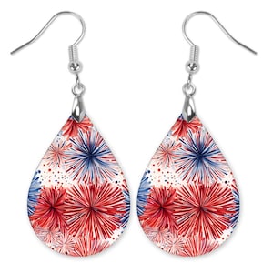 May include: A pair of teardrop-shaped earrings with a patriotic design. The earrings feature a white background with red and blue bursts of color, resembling fireworks. The earrings have silver-colored hooks.