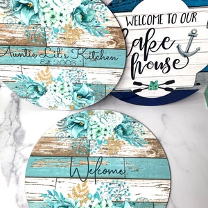 Pu&ograve; includere: Tre cartelli rotondi in legno con sfondo a venature di legno blu e bianco e disegni floreali. I cartelli recitano "Auntie Lil's Kitchen Est 2003", "Benvenuti alla nostra casa sul lago" con un'ancora e "Benvenuti".