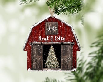 May include: A red barn-shaped Christmas ornament featuring a snowy roof, the year 2026, and the names Neal & Edie printed in white. The barn doors are open to reveal a lit Christmas tree inside, with white snowflakes falling across the entire design.
