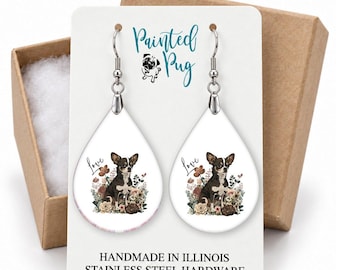 May include: Teardrop-shaped earrings featuring a black and white Chihuahua illustration surrounded by flowers and the word Love. The white display card reads Painted Pug, Handmade in Illinois, and Stainless Steel Hardware.