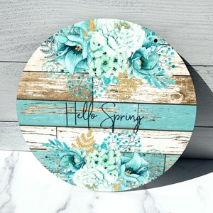 Pu&ograve; includere: Un cartello rotondo in legno con un design floreale blu e bianco e il testo "Hello Spring".