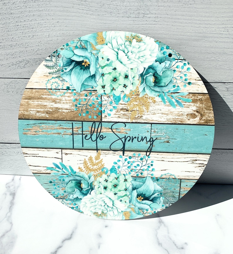 Pu&ograve; includere: Un cartello rotondo in legno con un design floreale blu e bianco e il testo "Hello Spring".