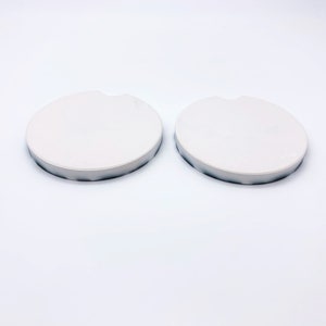 May include: Two white round ceramic coasters with a slightly raised edge.
