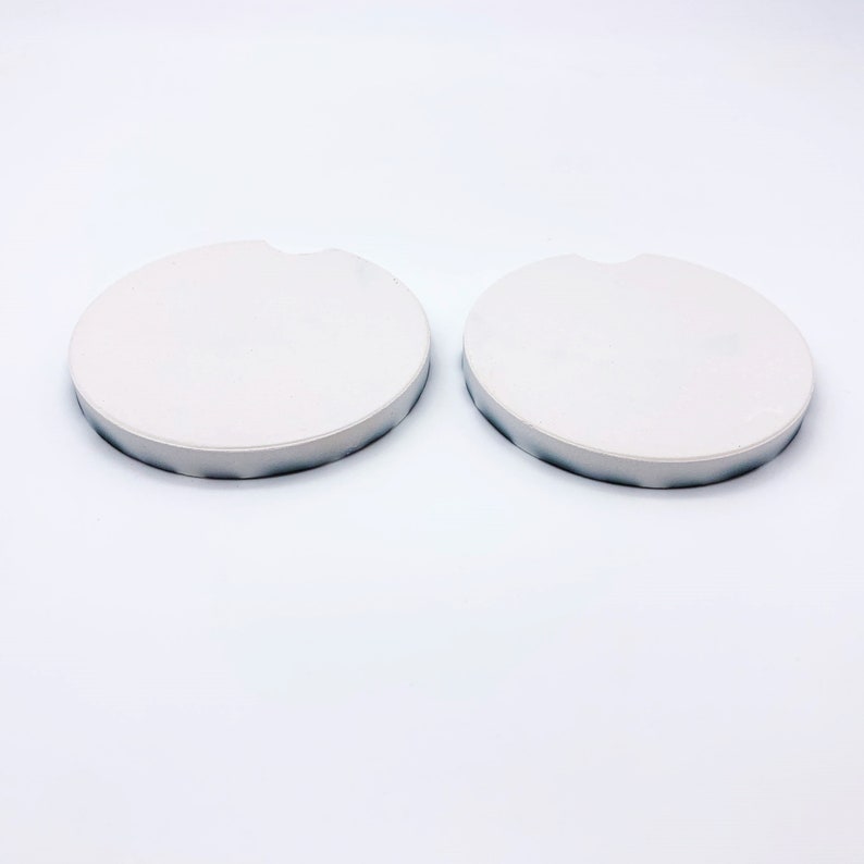May include: Two white round ceramic coasters with a slightly raised edge.