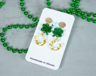 Könnte beinhalten: Grün glitzernde Kleeblatt- und gold glitzernde Hufeisen-Ohrringe. Die Ohrringe befinden sich auf einer weißen Karte mit dem Text "Printed Pug" und "Handmade in Illinois".