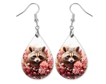 May include: A pair of silver teardrop-shaped earrings with a white background and a raccoon face surrounded by pink flowers.