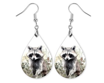 May include: A pair of silver teardrop-shaped earrings with a watercolor illustration of a raccoon in a forest setting.