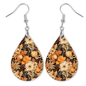 May include: A pair of teardrop-shaped earrings with a floral pattern. The earrings are made of metal and have a silver finish. The floral pattern features orange, yellow, and white flowers on a black background.