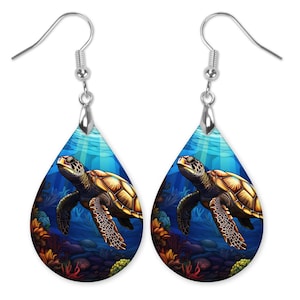 May include: A pair of teardrop-shaped earrings featuring a colorful illustration of a sea turtle swimming in a blue ocean with coral reefs. The earrings are made of metal with silver hooks.