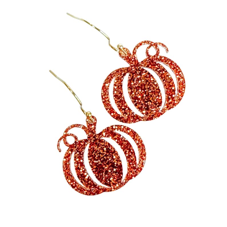 May include: A pair of dangle earrings featuring pumpkin-shaped charms covered in orange glitter. Each pumpkin charm has a small curled stem at the top and is attached to a thin gold-toned metal ear wire hook for hanging from the earlobe.